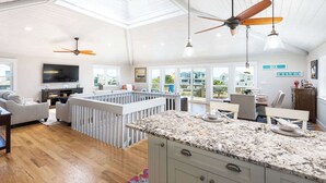 A spacious living area with a TV, seating, and a kitchen with granite countertops. - Newly Renovated Semi-Oceanfront Duck Home w/Pool (Duck)