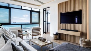 A modern living room with a large TV, comfortable seating, and a view of the ocean. - Magical Apartment w/Uninterrupted Ocean Views (Mouille Views) (Cape Town)