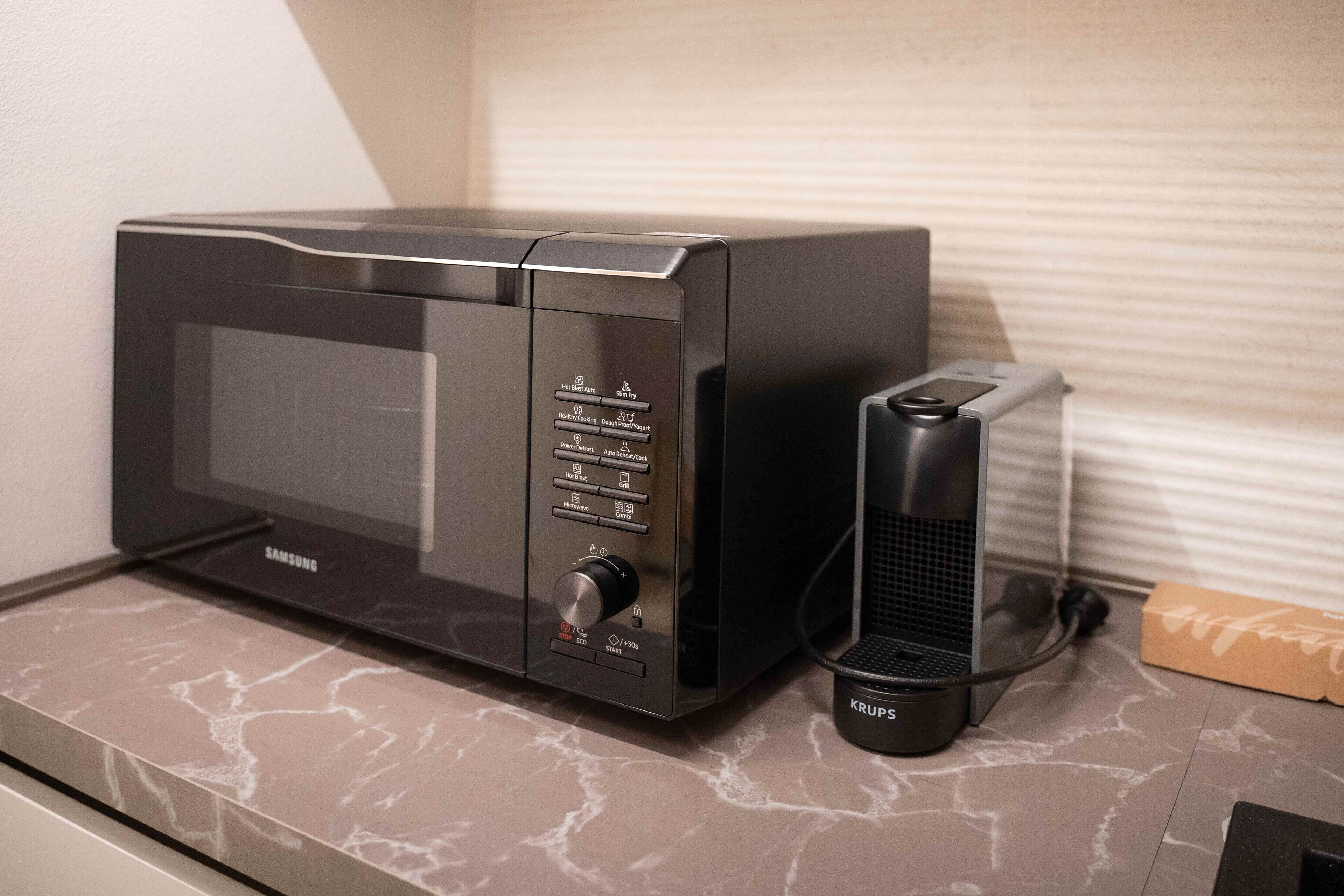 A Samsung microwave with a control panel and a Krups coffee maker on a marble countertop.