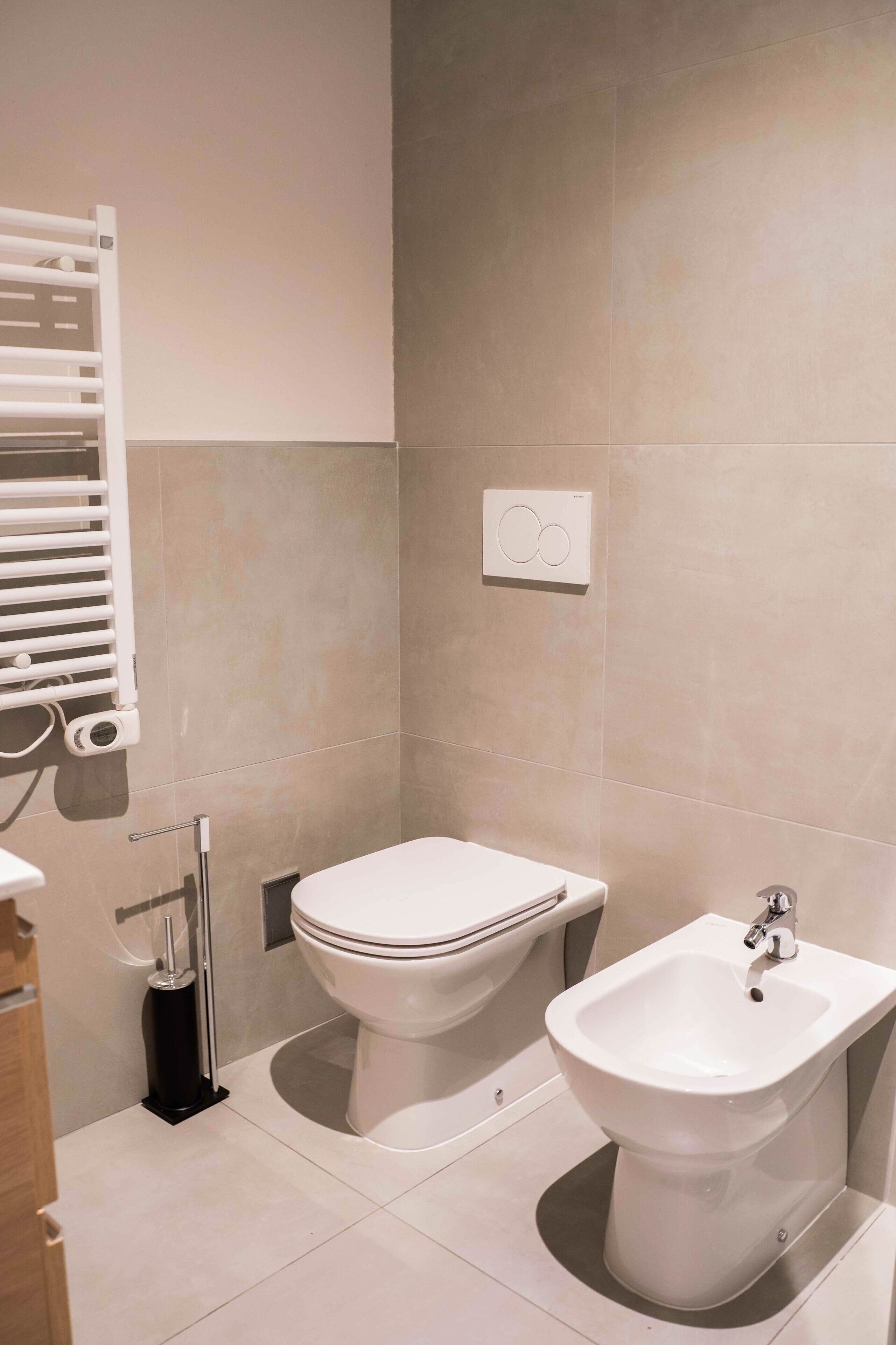 A modern bathroom with a toilet, bidet, and a towel rack.