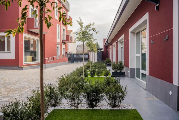 A courtyard with red buildings, a central tree, and a well-maintained garden.
