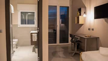 Habitación de hotel con cama, escritorio, silla, televisor, ventana, inodoro y ducha.