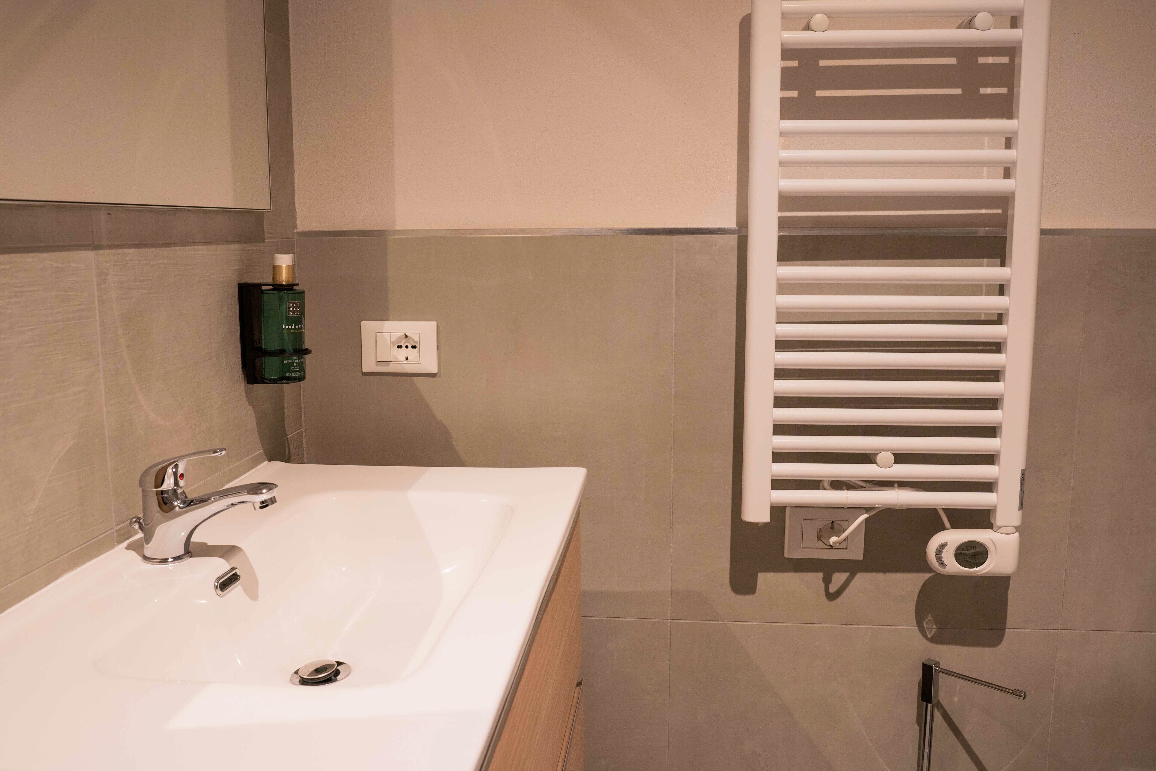 A bathroom with a white sink, a modern faucet, a towel rack, and a bottle of hand soap on the wall.