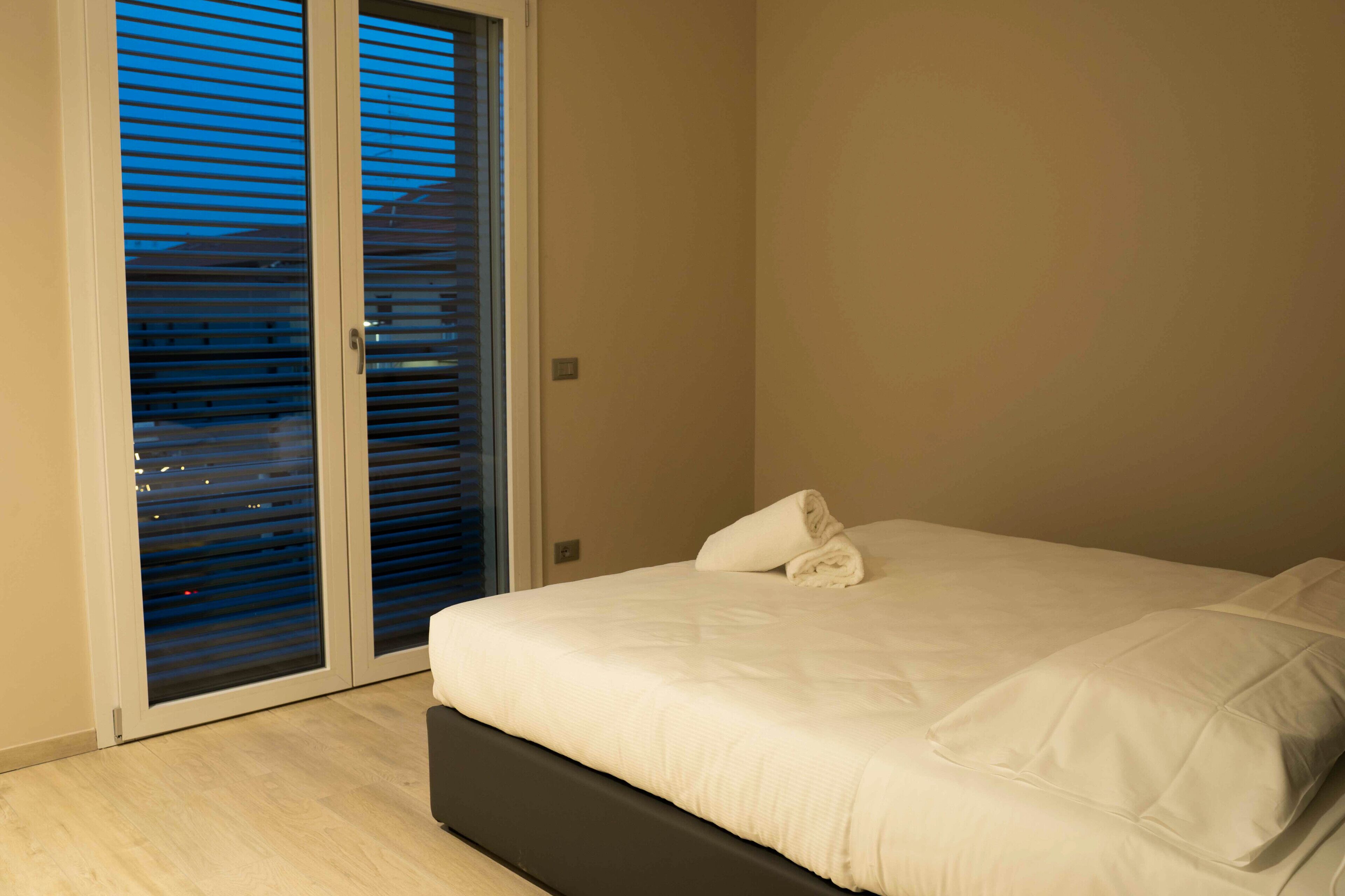A bedroom with a bed, a window with blinds, and a door.