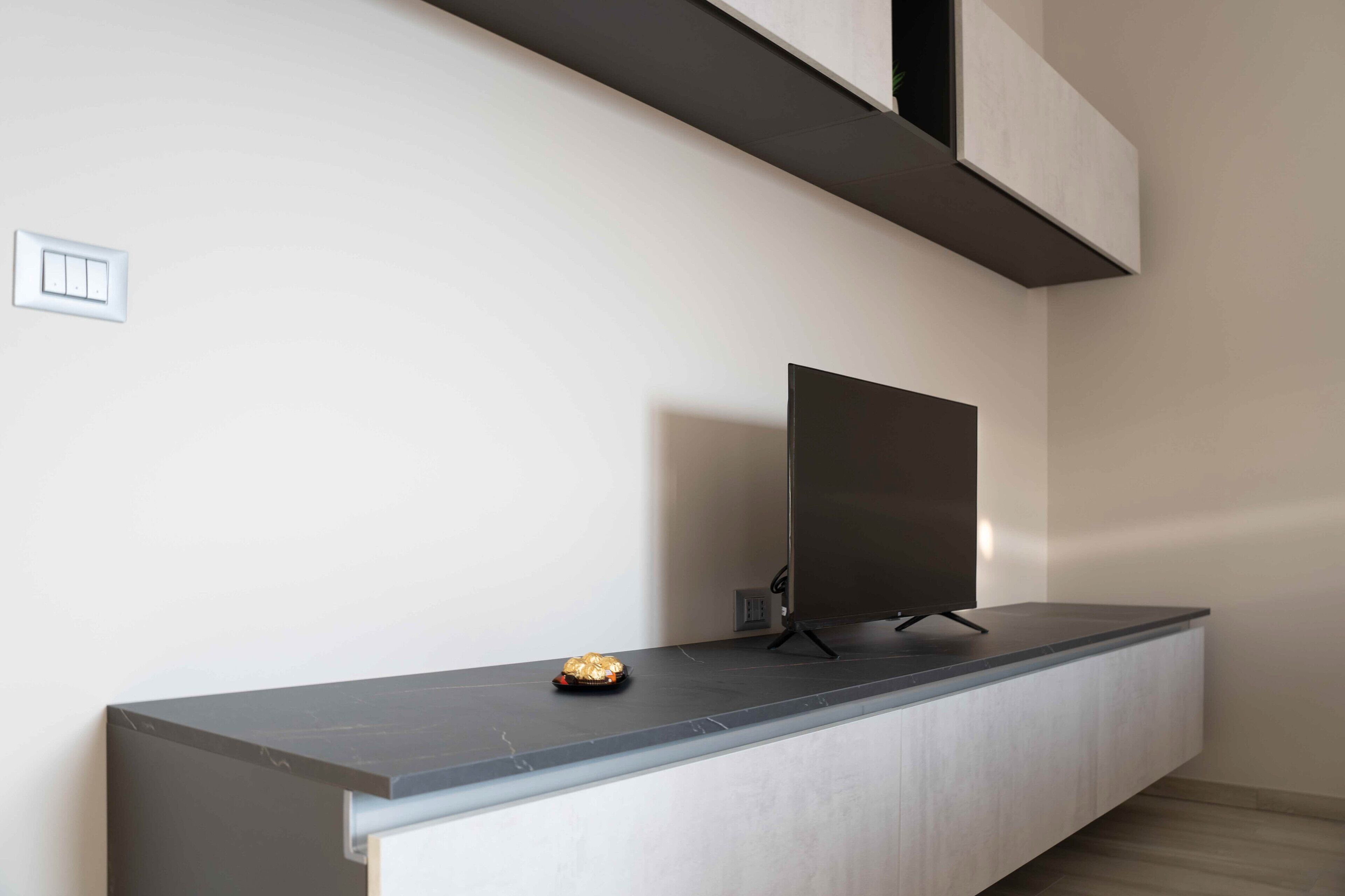 A modern living room with a flat-screen TV mounted on a wall, a small table with a decorative item, and a minimalist design.