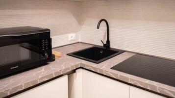 A kitchen with a black microwave, a black sink, and a marble countertop.