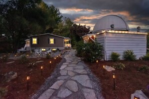 Una casa con un vialetto in pietra che conduce a un osservatorio a forma di cupola, circondata da alberi e illuminazione esterna.