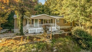 A single-story house with a porch, surrounded by trees and a garden. - 40 Acres w/Waterfalls, Vineyard, Stream, 5 bedroom (Moravian Falls)