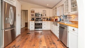 A modern kitchen with white cabinetry, stainless steel appliances, and a wooden floor. - 40 Acres w/Waterfalls, Vineyard, Stream, 5 bedroom (Moravian Falls)