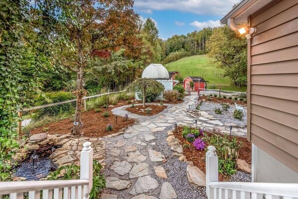 Un vialetto in pietra conduce a una casa con un giardino, uno stagno e una serra.
