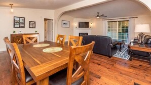 A spacious living room with a fireplace, a dining area with a wooden table and chairs, and a large window with curtains. - 40 Acres w/Waterfalls, Vineyard, Stream, 5 bedroom (Moravian Falls)