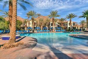 A pool area with blue lounge chairs, palm trees, and a mountain backdrop.