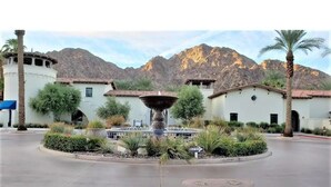A courtyard with a central fountain, surrounded by buildings with Mediterranean-style architecture, set against a mountainous backdrop. - Perfect View, Convenient and Peaceful King Casita at Legacy Villas (La Quinta)