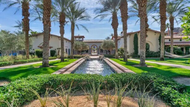 A courtyard with a central water feature, surrounded by palm trees and a building with a tiled roof. - Perfect View, Convenient and Peaceful King Casita at Legacy Villas (La Quinta)