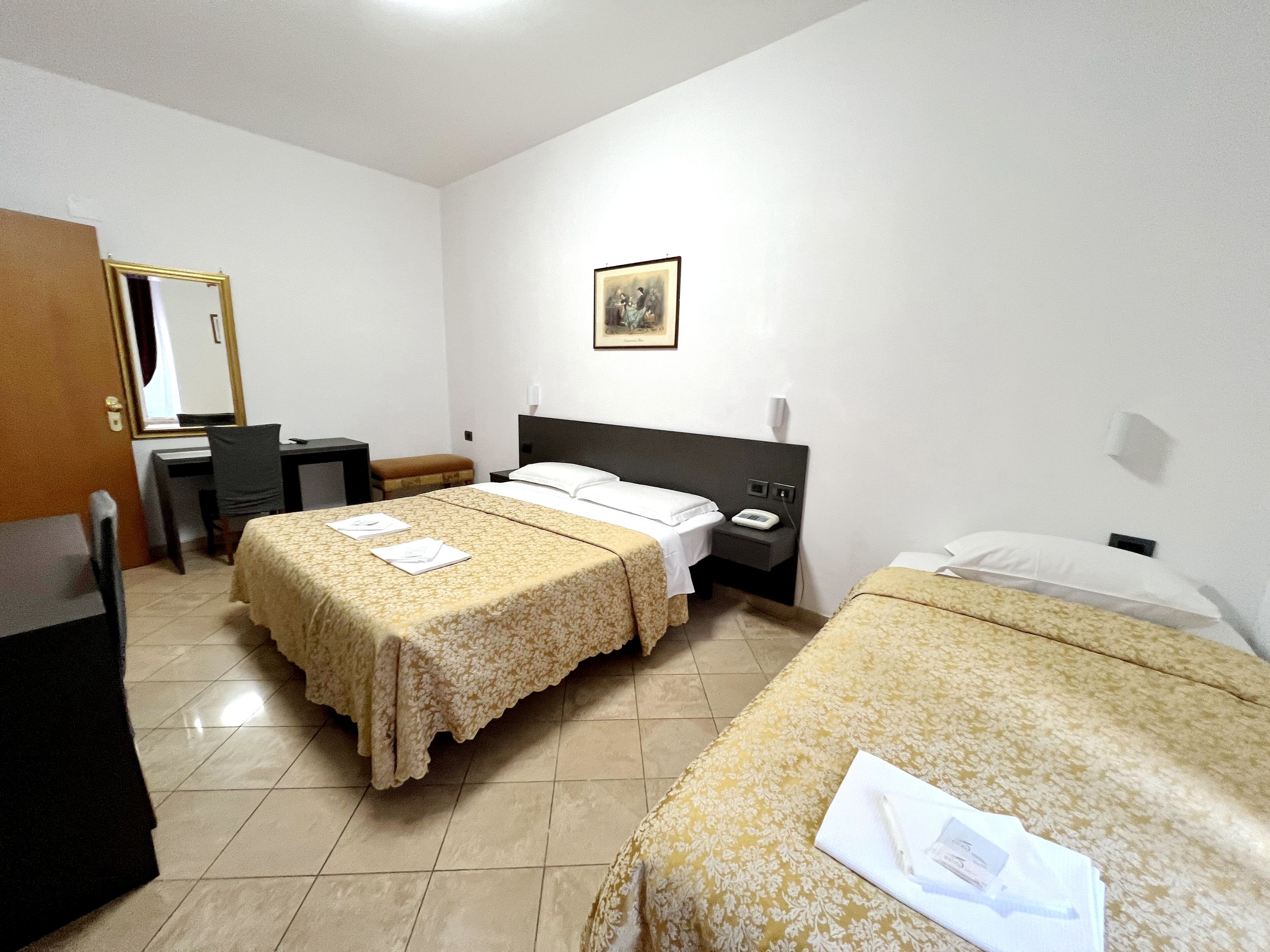 Camera d'albergo con due letti singoli, una scrivania, una sedia, un tavolino, uno specchio e un telefono fissato al muro.