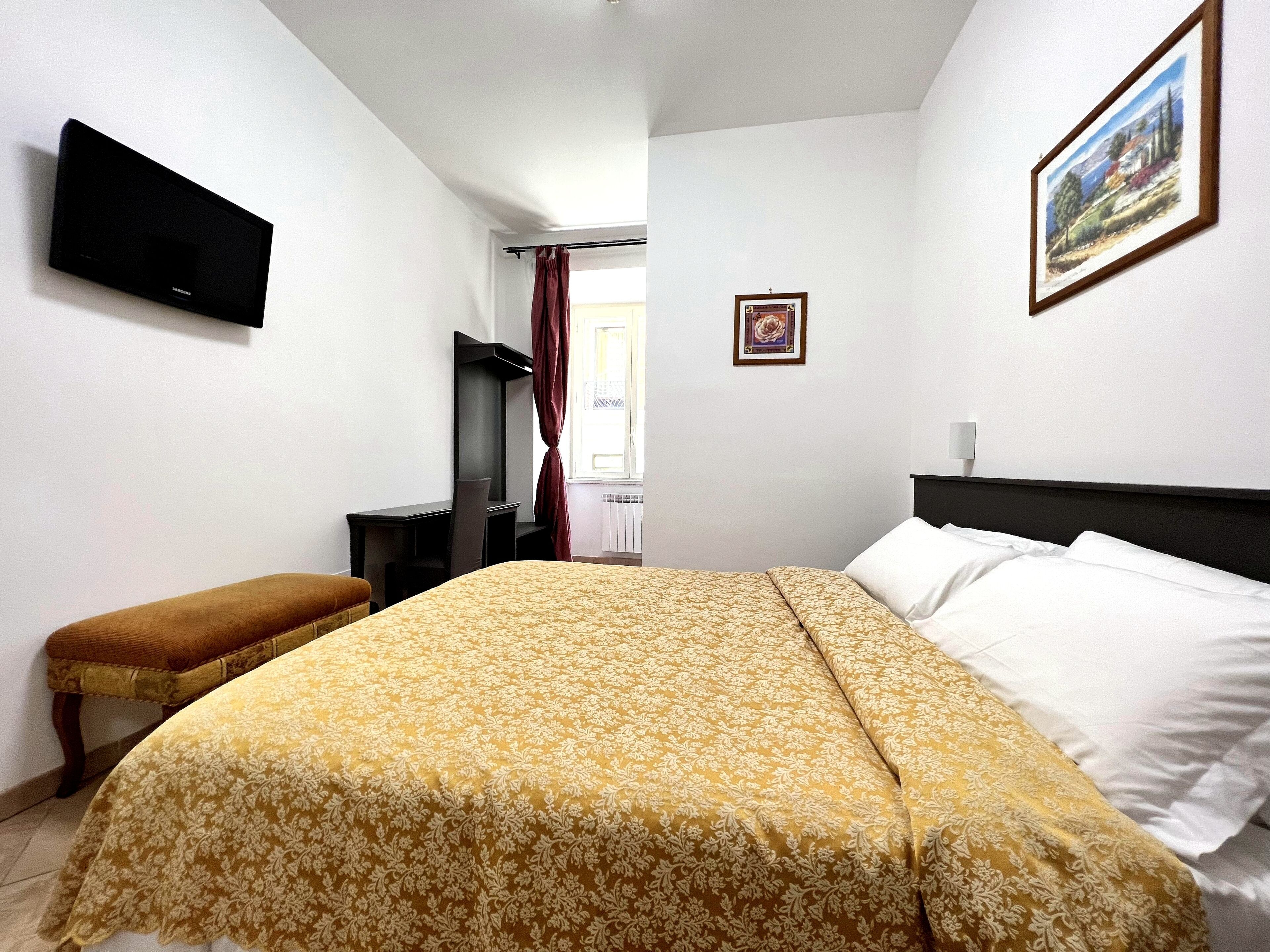 A bedroom with a bed, a desk, a chair, a television, and a framed picture on the wall.