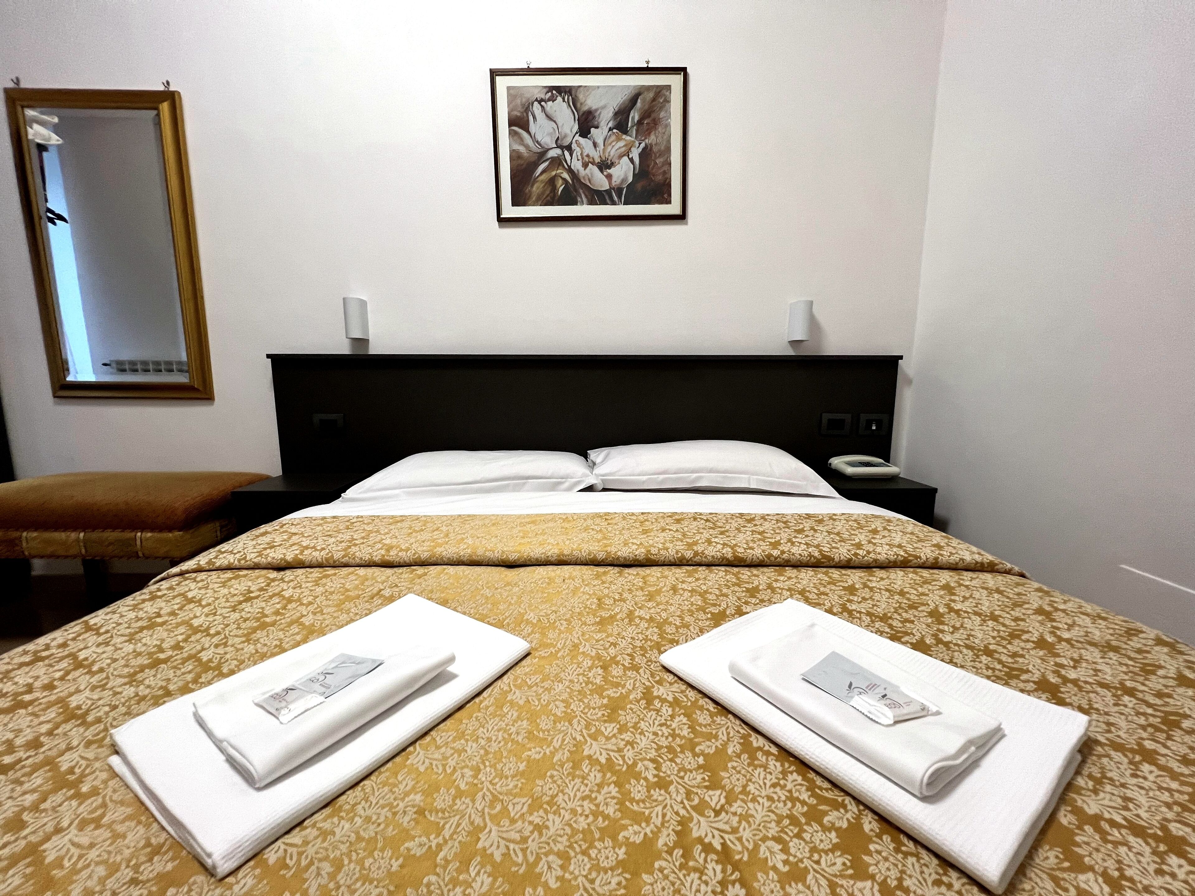 Una habitación de hotel con una cama, dos almohadas, una mesita de noche, un espejo y una obra de arte enmarcada en la pared.