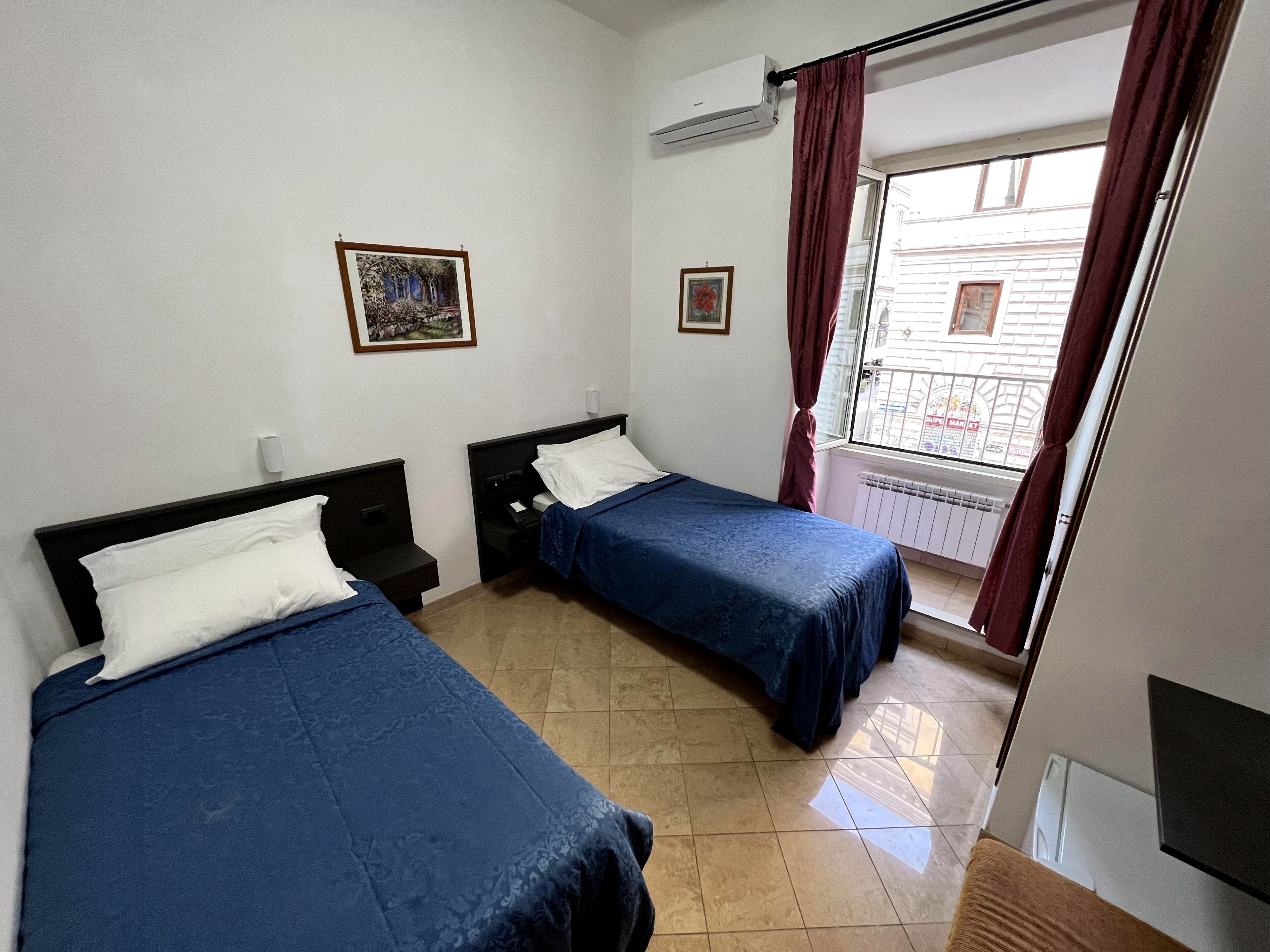 A hotel room with two beds, a window with curtains, and a radiator.