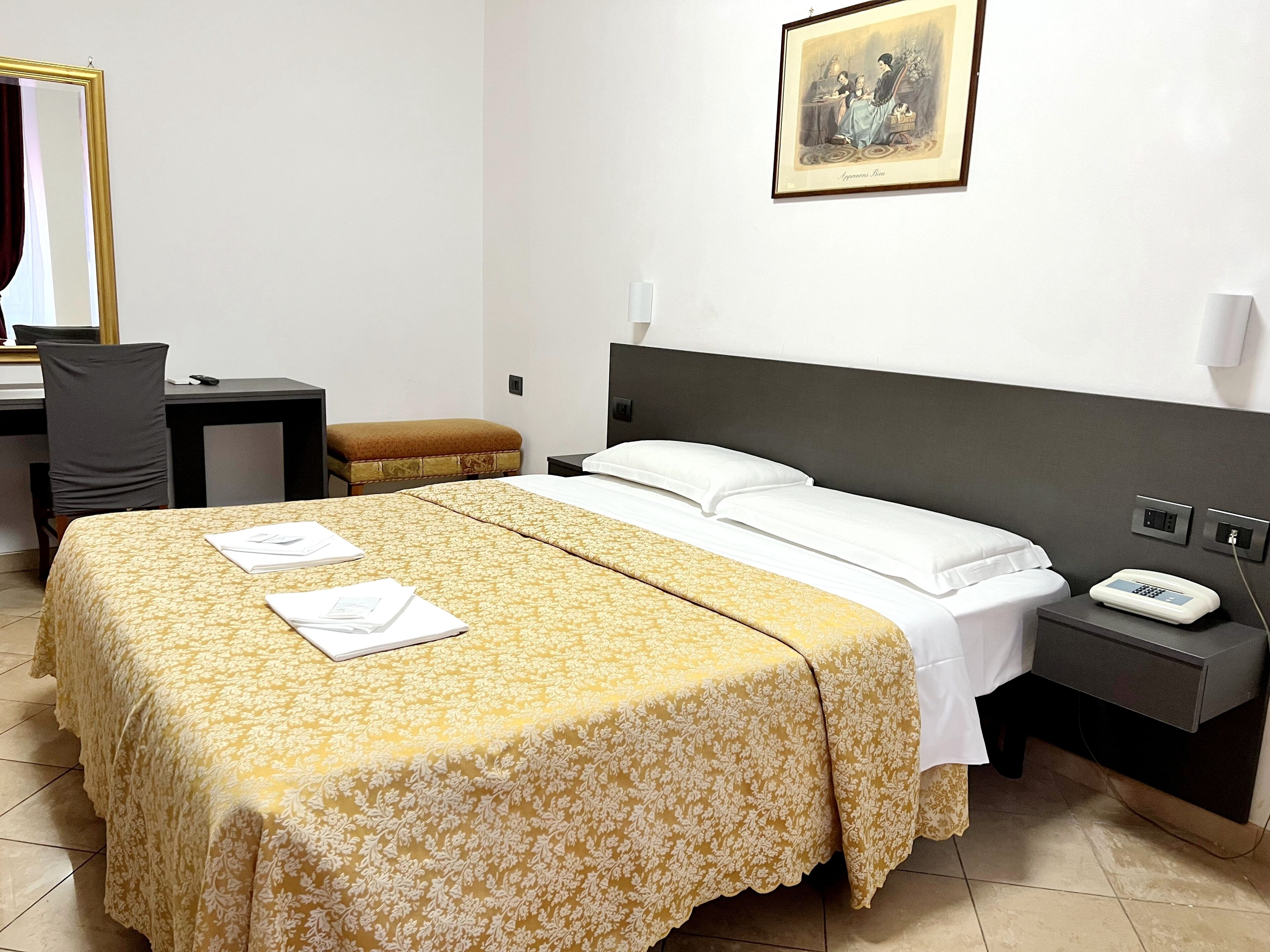 Une chambre d’hôtel avec un lit, un bureau, une chaise, une table de chevet et un tableau au mur.