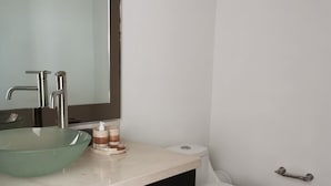 Un baño moderno con un espejo grande, un lavabo de vidrio, un inodoro y armarios oscuros.