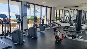 Un gimnasio con diverso equipo de ejercicio, ventanas amplias y vista al océano.