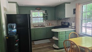 A kitchen with green cabinets, a black refrigerator, a sink, a stove, and a dining table with chairs.