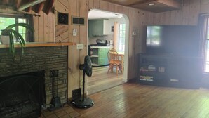 A wooden interior with a fireplace, a fan, a TV, and a kitchen area.
