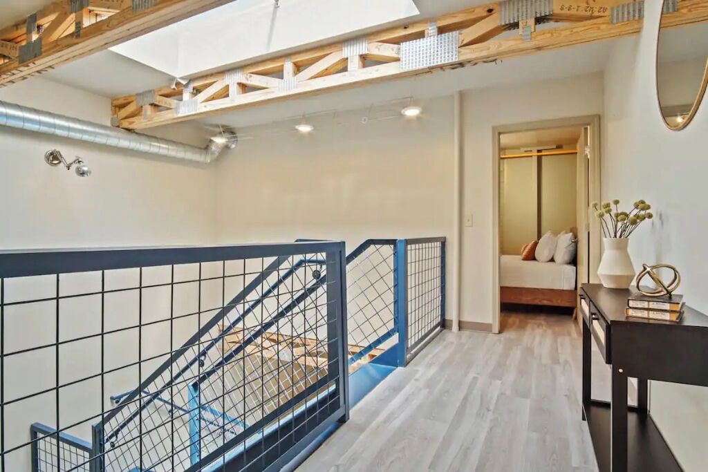 Un interno moderno con una scala, travi in legno e un letto sullo sfondo.