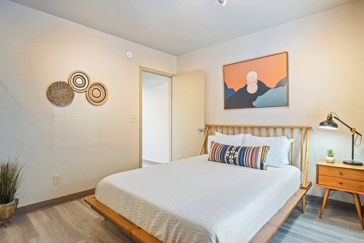 Ein Schlafzimmer mit Bett, Nachttisch, Lampe, Wandbildern und dekorativen Wandgestaltungen.