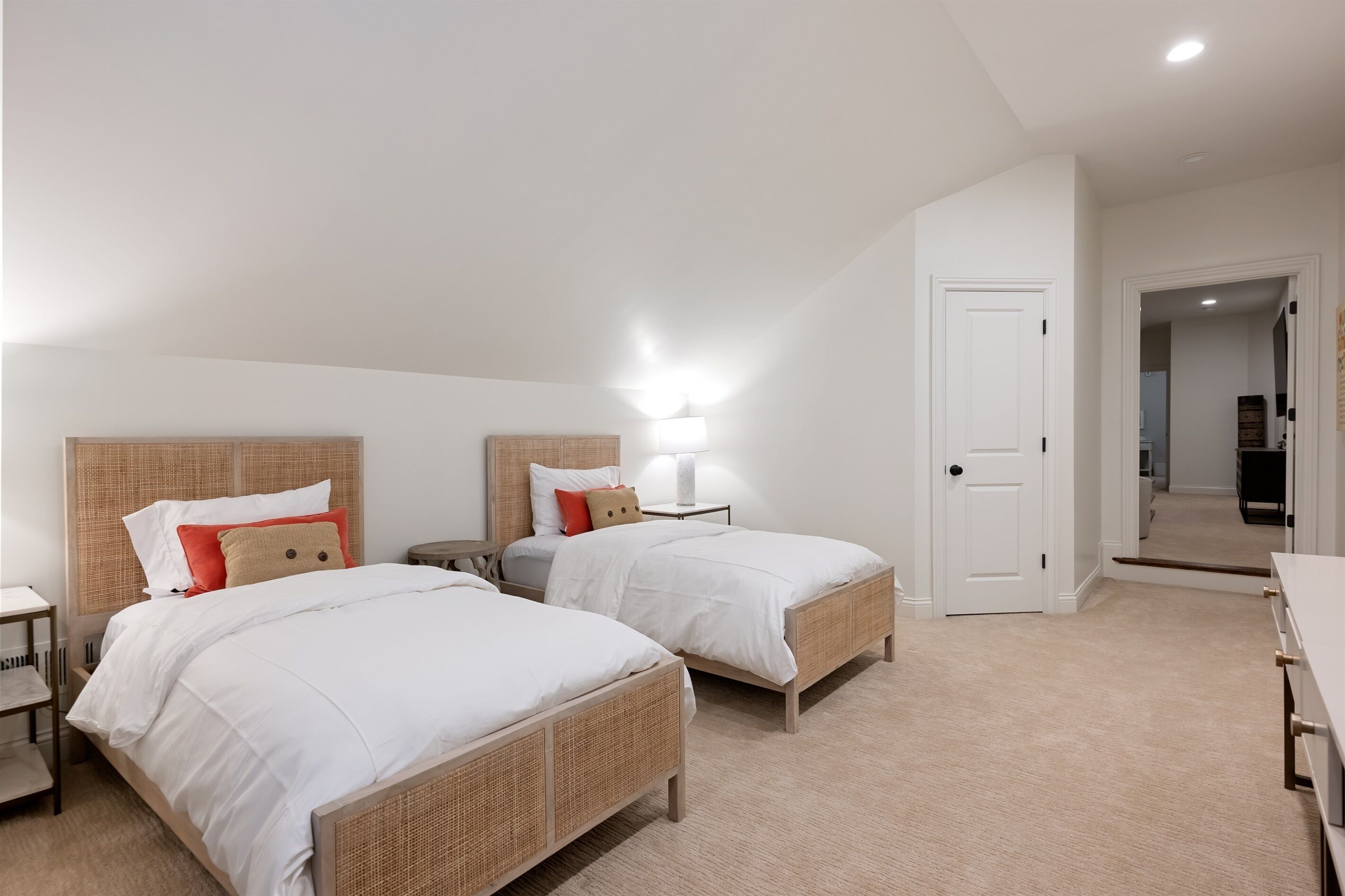 Une chambre avec deux lits, une table de chevet, une lampe et une porte donnant sur une autre pièce.