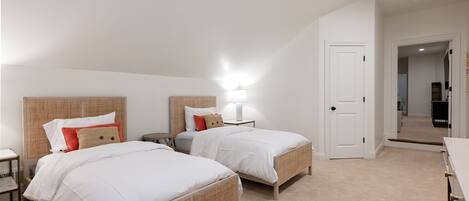 Une chambre avec deux lits, une table de chevet, une lampe et une porte donnant sur une autre pièce.
