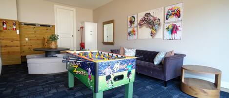 A room with a foosball table, a sofa, a coffee table, and wall art.
