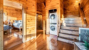 A wooden cabin interior with a washing machine, a bed, and a staircase.