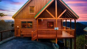 A wooden cabin with a steeply pitched roof, a porch with a railing, and a sign reading "Welcome to Jolene."