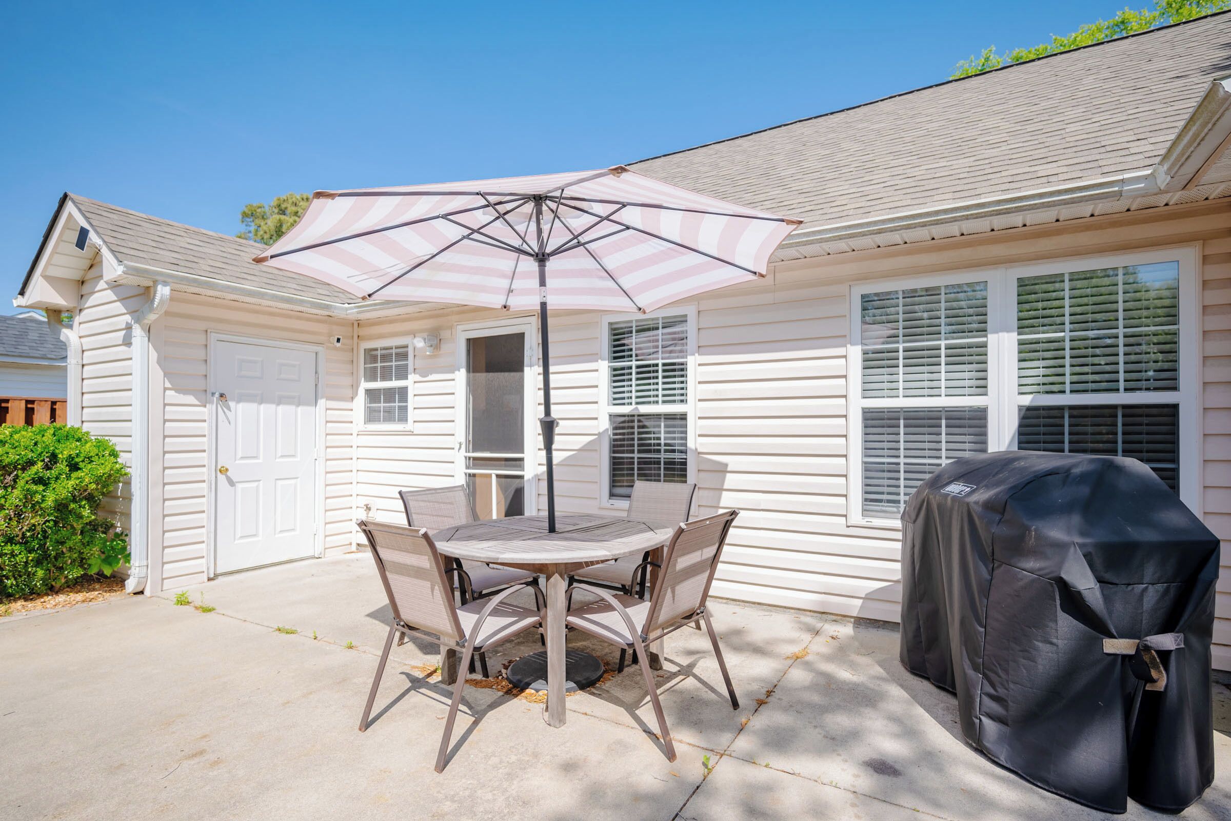 Une terrasse avec une table et des chaises, un parasol et une housse pour barbecue.
