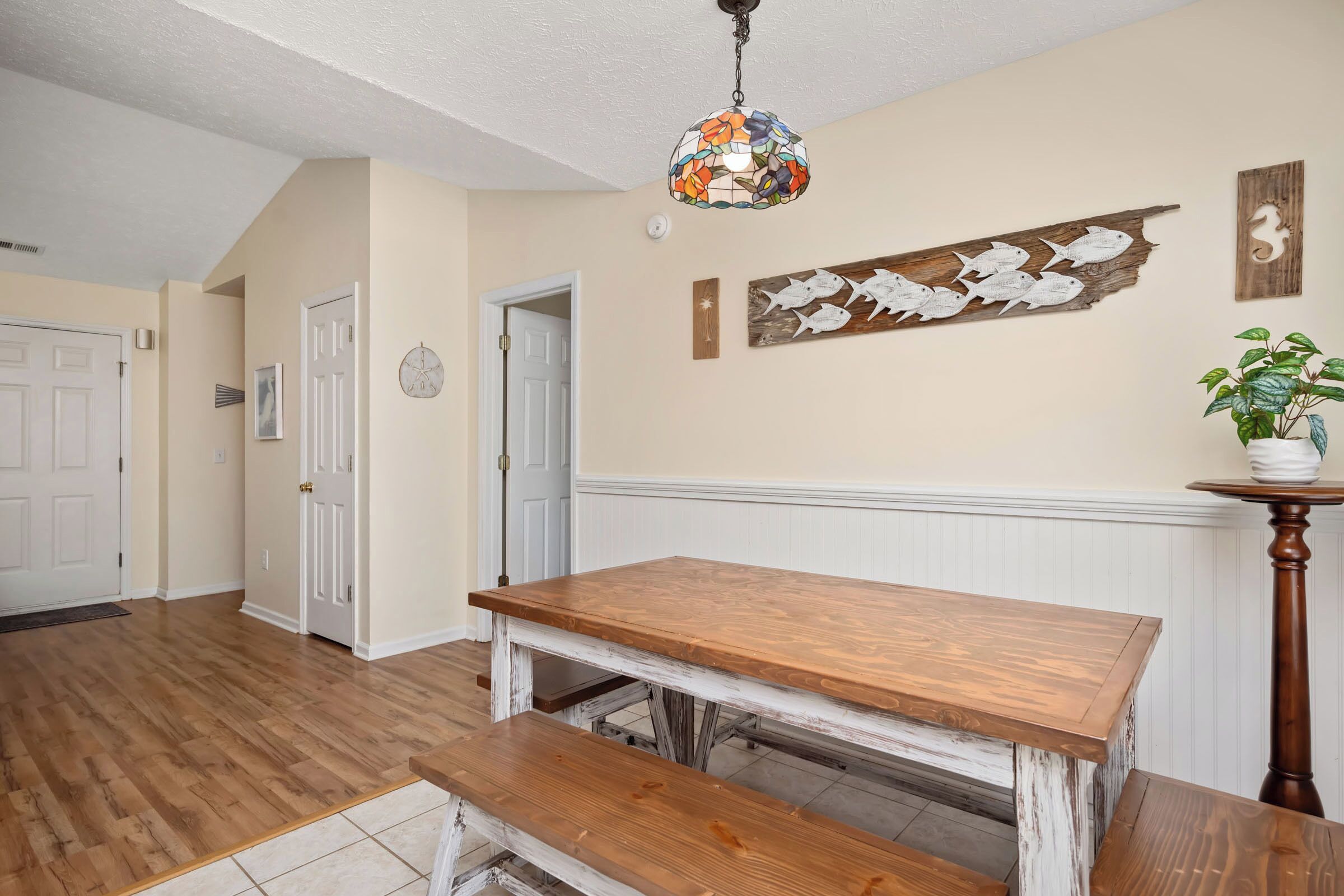 A dining area with a wooden table and bench, a decorative fish wall art, and a hanging light fixture.