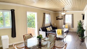A dining area with a glass table surrounded by wicker chairs, a sofa with patterned cushions, and a ceiling fan. - Cheerful Bahamian Pad. Walk to Beaches, Bars, Restaurants, Grocery-Liquor stores (hatchet bay)