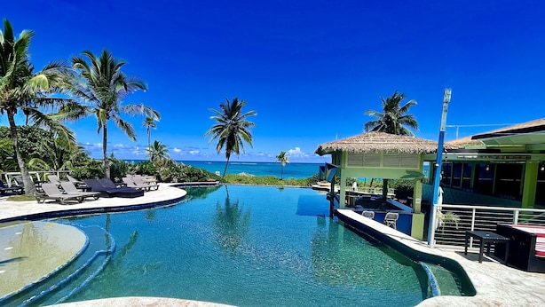 A swimming pool with lounge chairs, palm trees, and a view of the ocean. - Cheerful Bahamian Pad. Walk to Beaches, Bars, Restaurants, Grocery-Liquor stores (hatchet bay)