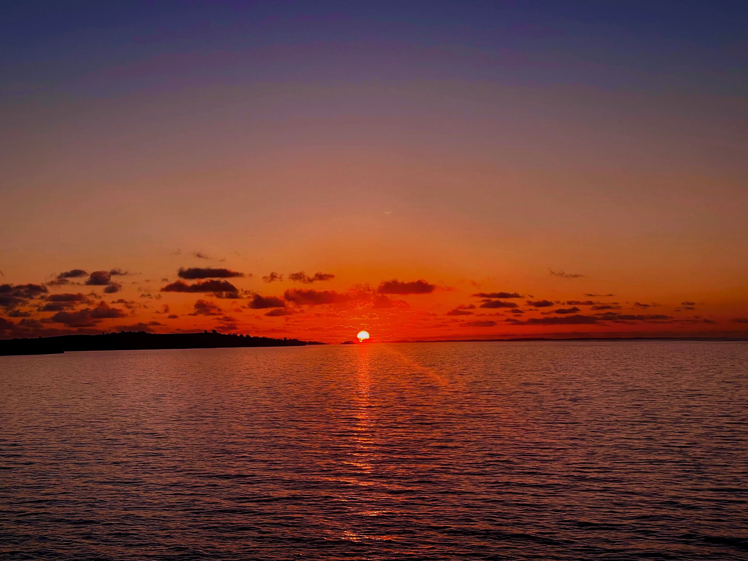 A sunset over a calm body of water with a silhouette of land in the distance.