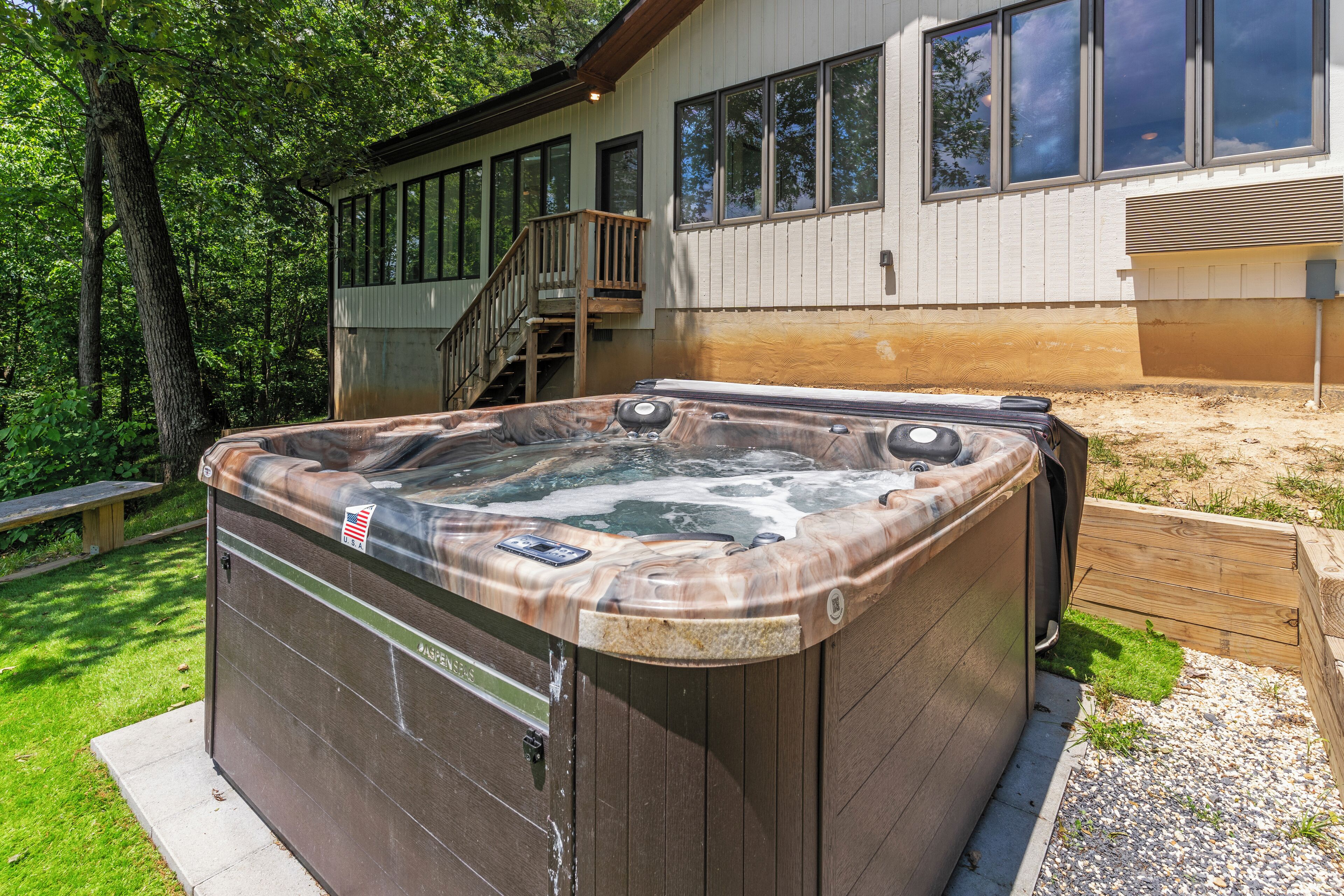 Una vasca idromassaggio in un giardino privato con una veranda in legno e una casa sullo sfondo.