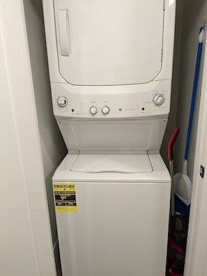 Eine Waschmaschine mit Frontlader, einer gelben Energieeffizienzklasse und einem an die Wand gelehnten Mop.