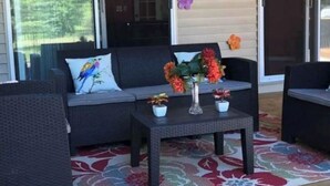 Un espace patio avec un canapé en osier foncé, une petite table agrémentée de plantes en pot et un tapis aux motifs floraux colorés.
