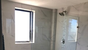 A modern bathroom with a glass-enclosed shower, a toilet, and a window providing natural light. - Departamentos MDR (Mazatlán)