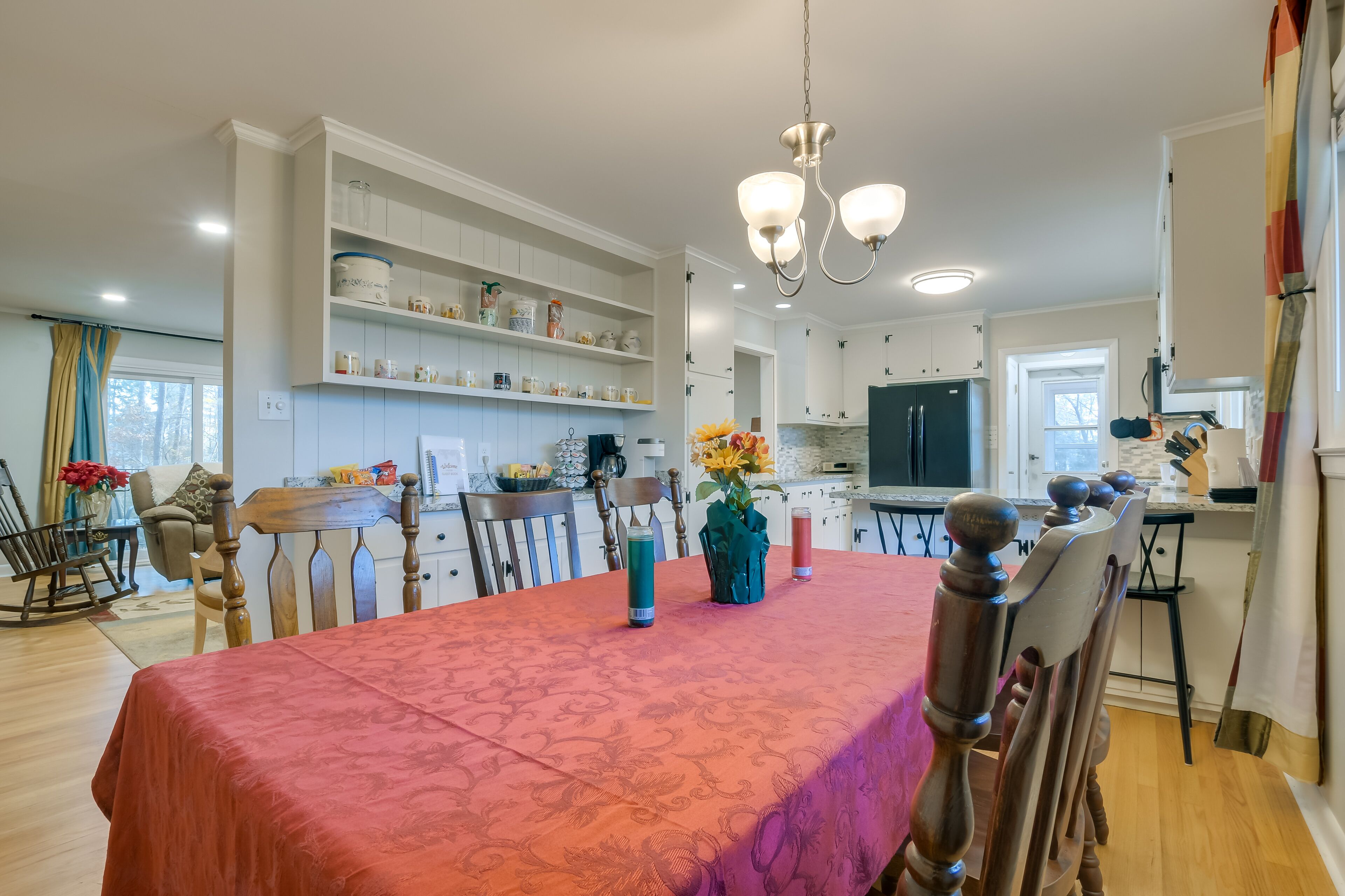 Un coin repas avec une table dressée pour quatre personnes, entourée de chaises en bois. Un lustre est suspendu au-dessus de la table, et un vase rempli de fleurs est posé sur la table.