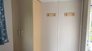 A room with a wardrobe, a bed, and a door with two coat hooks. - Mobile home 6 persons. (Attigny)