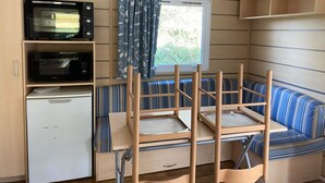 A compact RV interior with a kitchenette, a blue-striped sofa, and a window with curtains. - Mobile home 6 persons. (Attigny)