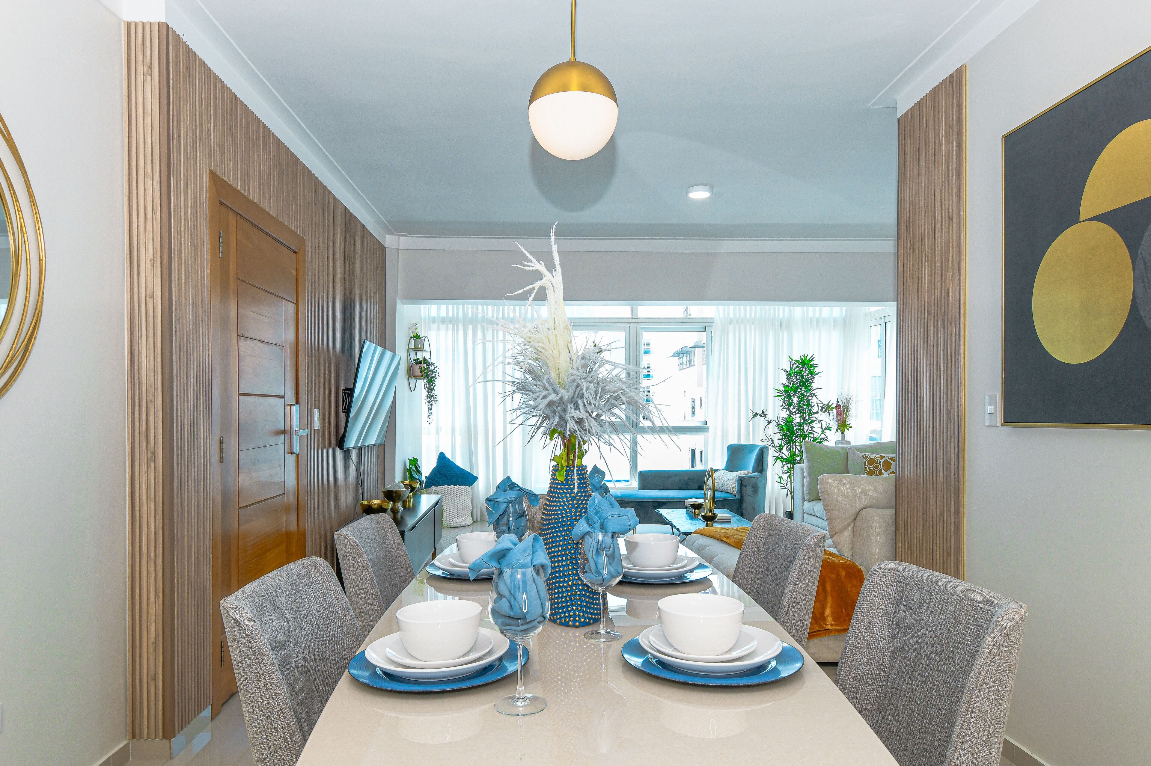 Comedor con una mesa redonda para cuatro personas, un jarrón con flores blancas e iluminación colgante moderna.