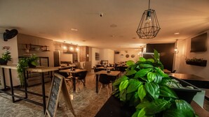 Cocina moderna con barra, mesas y sillas de madera. Hay plantas y un cartel de pizarra.