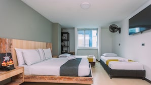 Habitación de hotel con una cama grande, una cama más pequeña, un escritorio con teléfono, una estantería y un televisor montado en la pared.