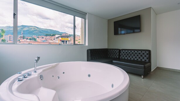 Un baño moderno con una bañera grande, un sofá negro y un televisor montado en la pared.